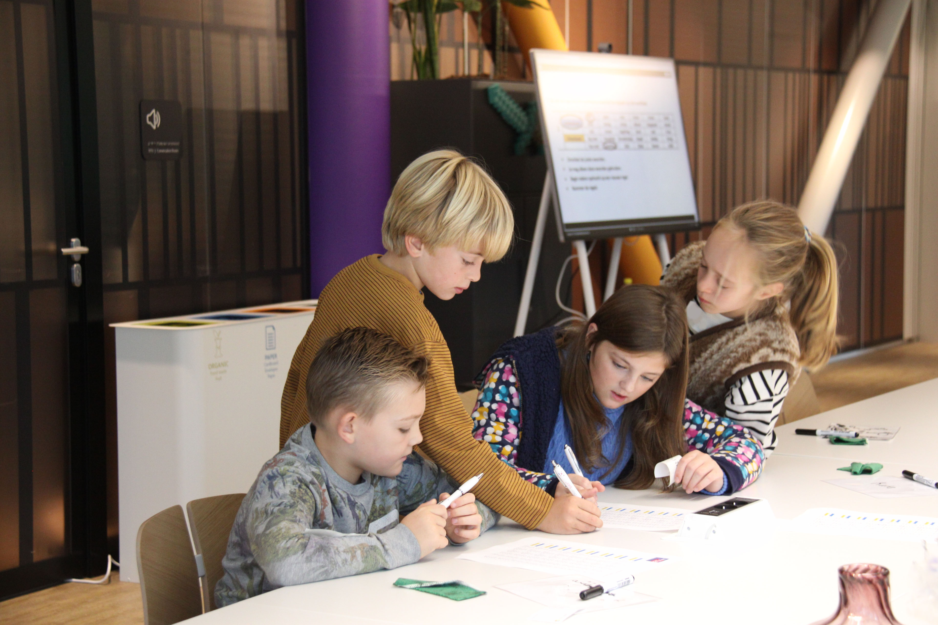 Een groep van vier kinderen aan een tafel, werkend aan een opdracht op stukken papier